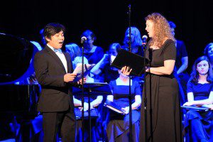 A man and woman sing in front of an audience.